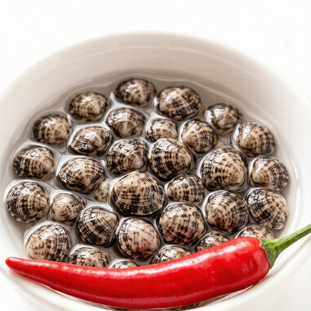 Raw thin-shell clams piled in a white bowl with a red chili beside them