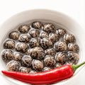 Raw thin-shell clams piled in a white bowl with a red chili beside them