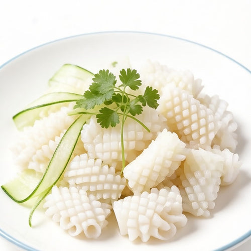 Raw cross-scored squid pieces in a white bowl with cucumber ribbons and coriander