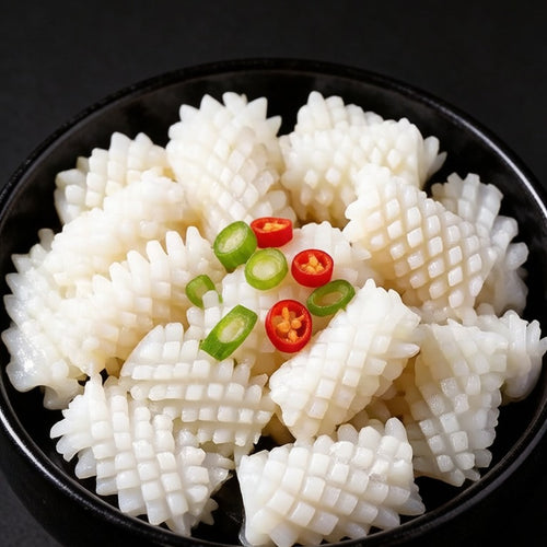 Blanched squid flowers curled into shape in a black bowl with green and red chili