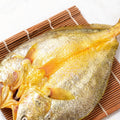 Whole golden croaker resting on a bamboo mat, its scales catching the light